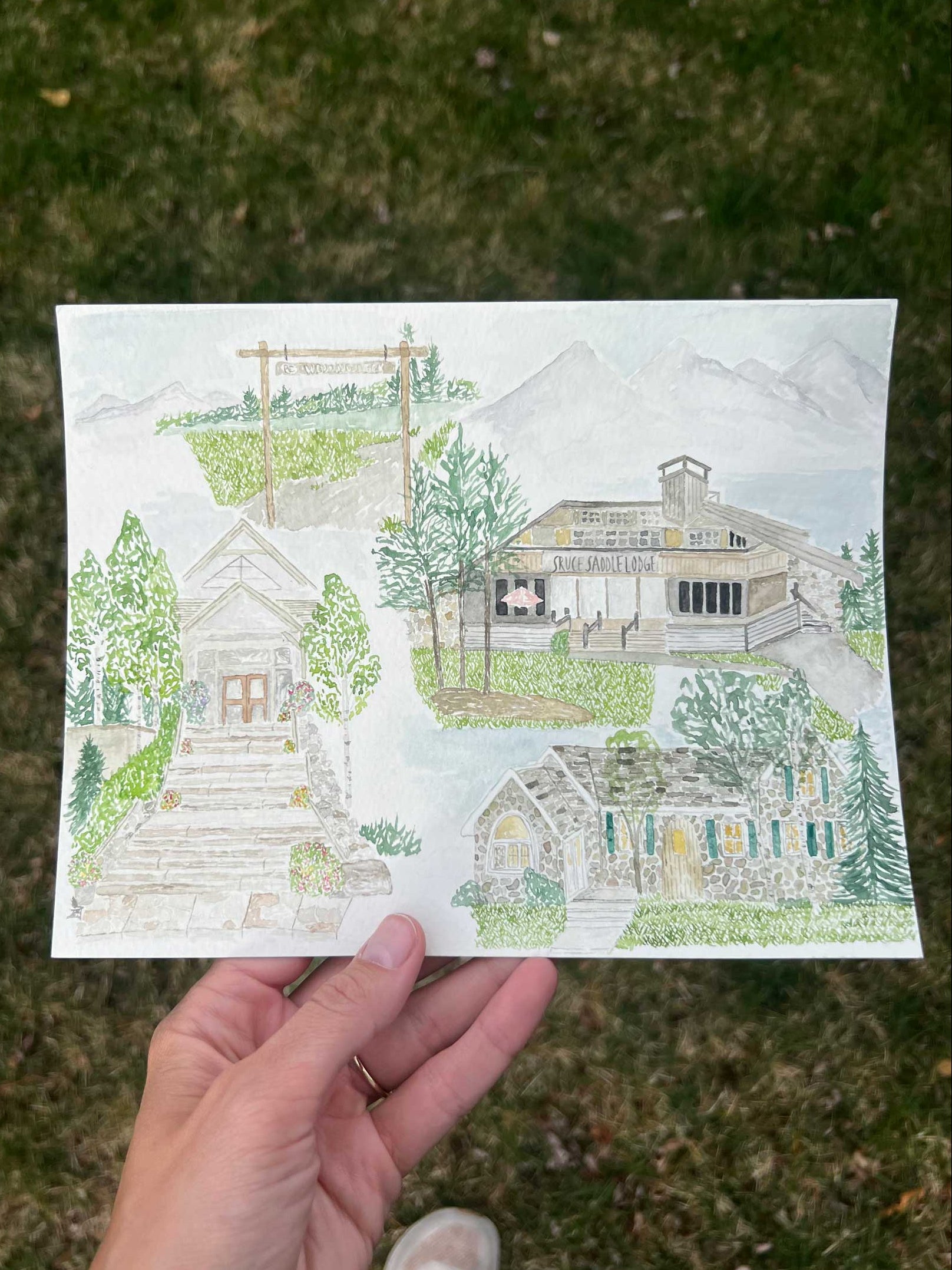 Hand holding a drawing of a house and garden on grass