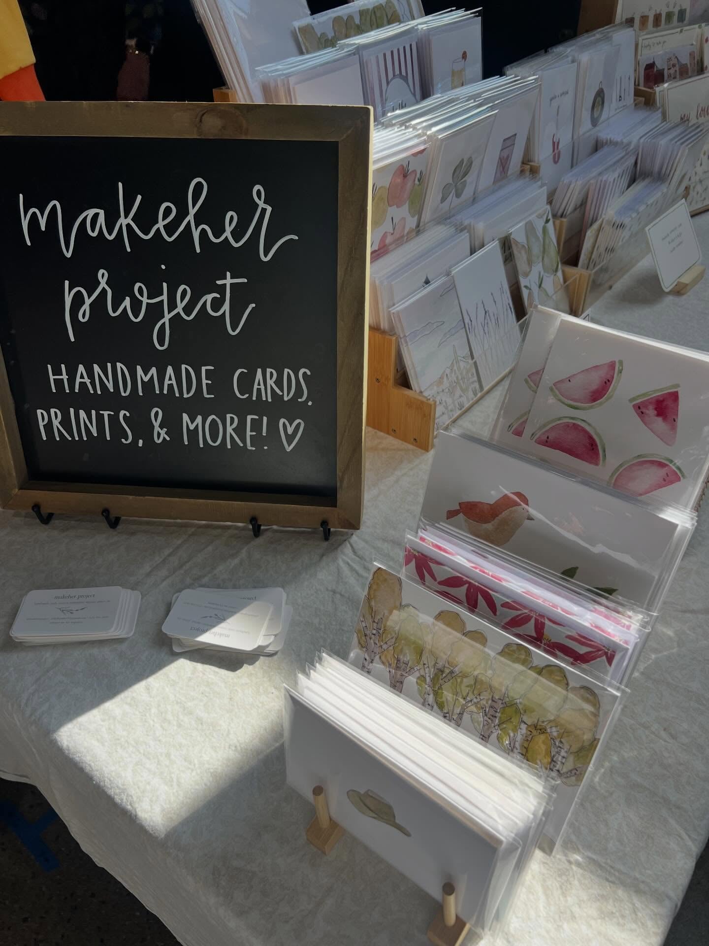 Makeher Project display with handmade cards and prints on a table during a market.