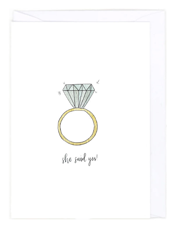 Card with a gold ring and a big diamond, and 'she said yes!' text on a white background